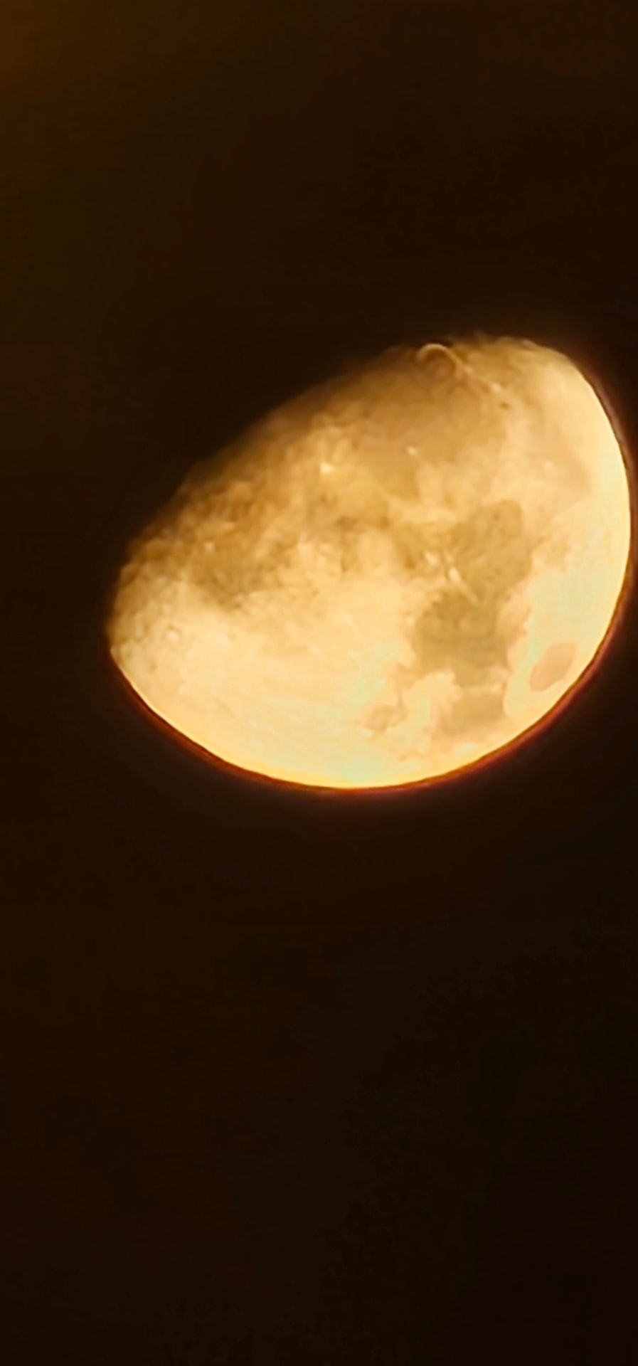 A warm golden Moon against a dark sky, with craters and darker areas visible on its illuminated surface.